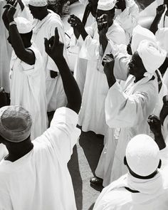 a group of men standing around each other in white outfits and hats, all holding their hands up