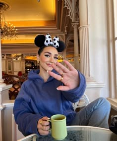 a woman sitting at a table with a coffee cup in front of her and mickey mouse ears on her head