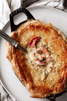 a white plate topped with a pie covered in meat and cheese sauce next to a knife