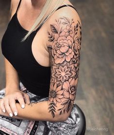 a woman sitting down with a flower tattoo on her arm and shoulder, looking at the camera