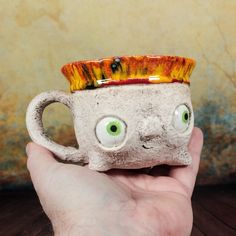 a hand holding a ceramic cup with eyes on it