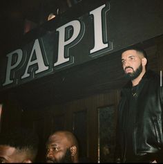 a man standing in front of a sign that says papi with other men around him