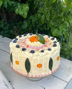 a white cake with oranges and blueberries on it sitting on a wooden table