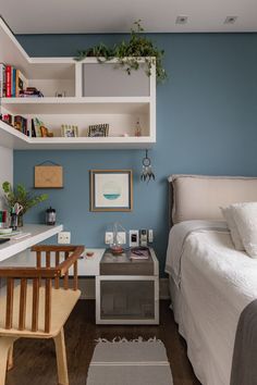 a small bedroom with blue walls and white bedding, bookshelf above the bed