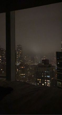 a view of the city lights at night from a bedroom in an apartment building with a large window