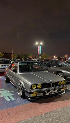 several cars parked in a parking lot at night with the lights on and one car is silver