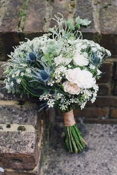 a bridal bouquet with white flowers and greenery on a brick wall in an alleyway