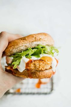 a hand holding a chicken burger with lettuce and tomato sauce