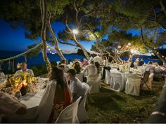 a group of people sitting around tables with white clothed cloths on them at night