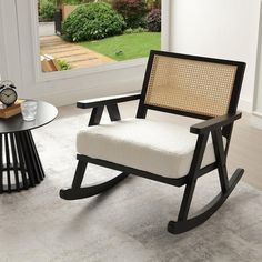 a rocking chair sitting on top of a white rug next to a table with a clock