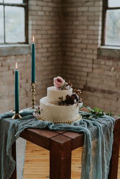 a wedding cake sitting on top of a wooden table next to two candles and flowers