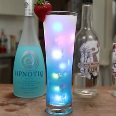 a glass filled with liquid and a strawberry sitting on top of a table next to bottles