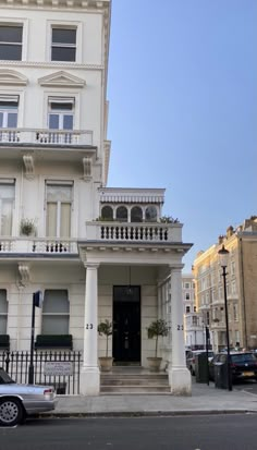 a car parked in front of a tall white building with balconies on the second floor