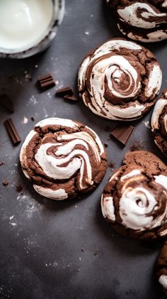 chocolate cookies with white frosting and chocolate chips on a black surface next to milk