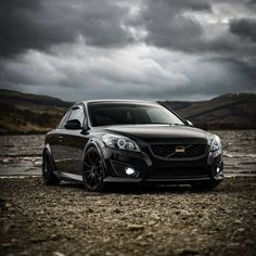 a black car parked on top of a dirt field next to a body of water