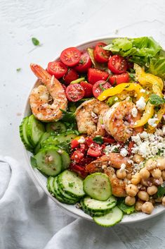 a salad with shrimp, tomatoes, cucumbers, and other vegetables in a white bowl