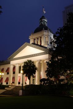 a large building lit up at night with palm trees in the foreground and an american flag on top