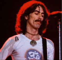 a man with long hair and mustaches playing an electric guitar in front of a microphone