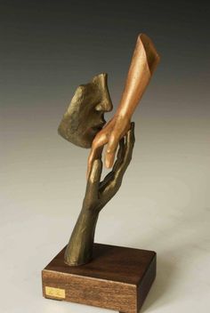 a bronze sculpture of a hand holding a piece of wood on top of a wooden base