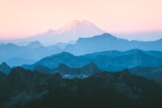 the mountains are covered in blue and pink hues as the sun sets over them