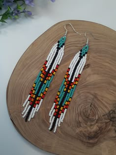 a pair of beaded earrings sitting on top of a wooden table next to flowers