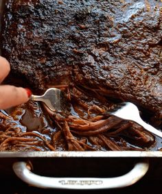 a person is holding a fork over some meat in a roasting pan with sauce on it