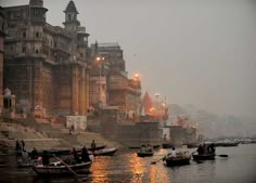 several boats floating on the water in front of old buildings at night with lights reflecting off them