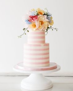 a pink and white striped cake with colorful flowers on top, sitting on a pedestal