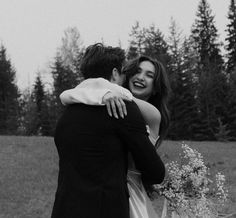 a man and woman hugging each other in a field with trees in the back ground