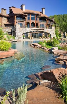 a large house sitting on top of a lush green hillside next to a body of water