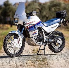 a white and blue motorcycle parked on top of a gravel road next to grass covered field