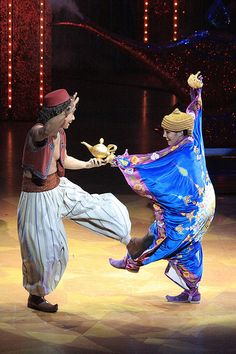 two people dancing on stage with lights in the background and one person holding a teapot