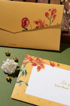 two yellow envelopes with red and orange flowers on them next to a white card