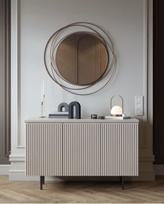 a white dresser with a round mirror on the wall above it and a lamp next to it