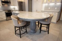 a kitchen with white cabinets and marble counter tops, two stools at the center of the table