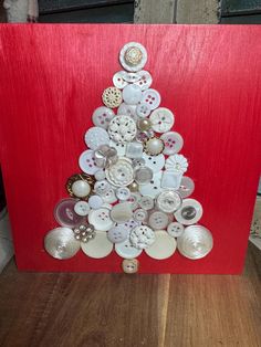 a christmas tree made out of buttons on a red board with a wooden floor and wall in the background