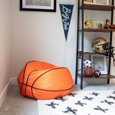 an orange basketball bean bag sitting on top of a white rug next to a book shelf