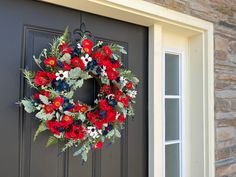 a wreath with red, white and blue flowers hangs on the front door