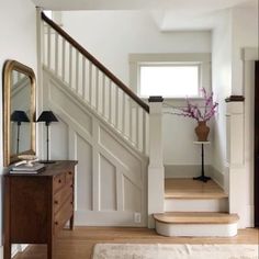 there is a mirror and some stairs in the house with flowers on the table next to it