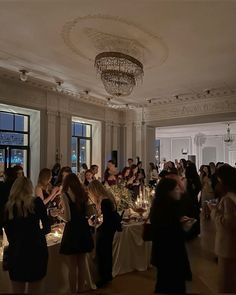 a group of people standing around a table in a room with chandeliers and windows