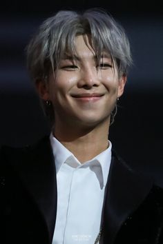 a man with grey hair wearing a white shirt and black blazer smiling at the camera