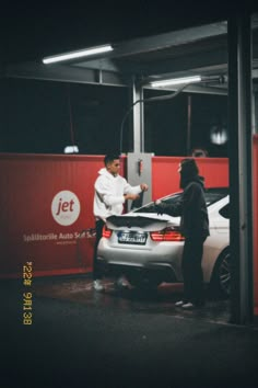 two people standing next to a car in a garage