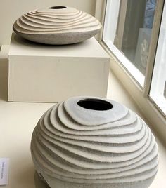 two white vases sitting on display next to each other in front of a window