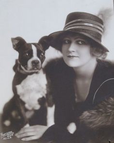 a black and white photo of a woman with a hat next to a small dog