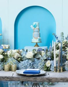 a table with blue and white flowers, candles and a cake on the table top