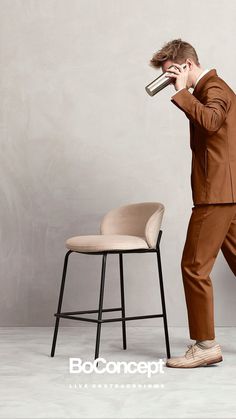 a man standing next to a chair and drinking from a cup in front of his face