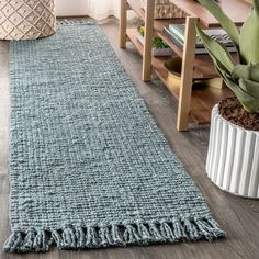 a blue rug with fringes on the floor in front of a wooden table and potted plant