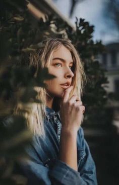 a woman standing in front of a tree with her hand on her chin and looking off into the distance