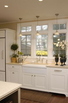 a kitchen with white cabinets and counter tops, two vases filled with flowers next to the sink