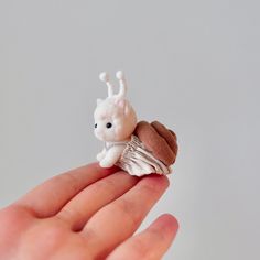 a tiny white and brown animal sitting on top of a person's hand in front of a gray background